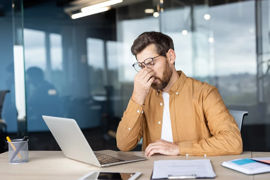 a man sitting at his desk at work massaging the bridge of his nose