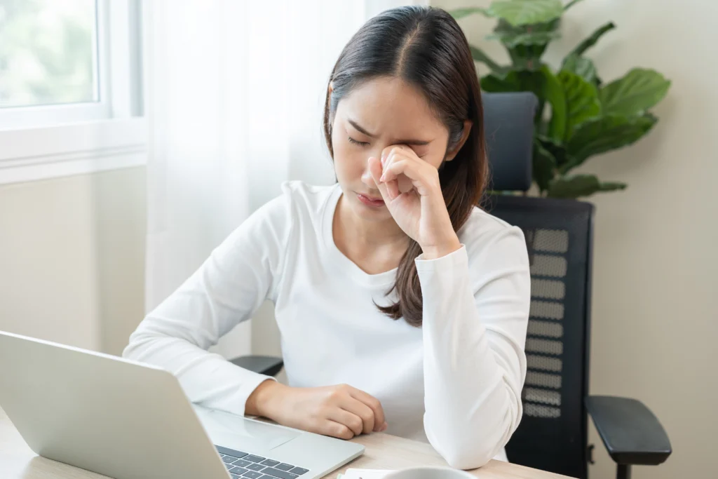 A woman working on a a laptop rubs her dry, tired eyes.
